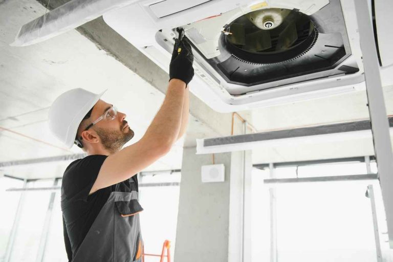 HVAC technician wearing safety gear installing a ceiling-mounted air conditioning unit in a commercial building.