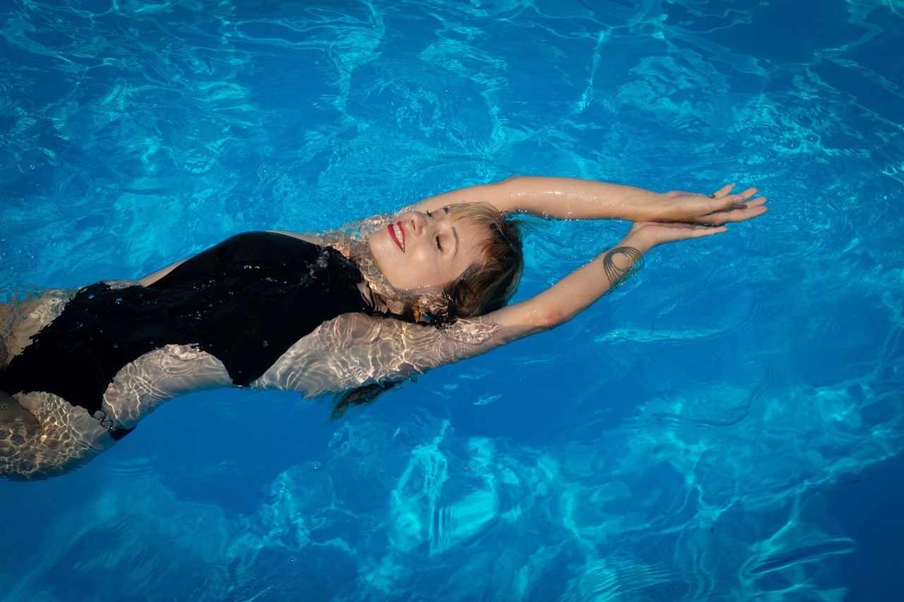 Woman relaxing and floating in a clear blue swimming pool under bright sunlight.