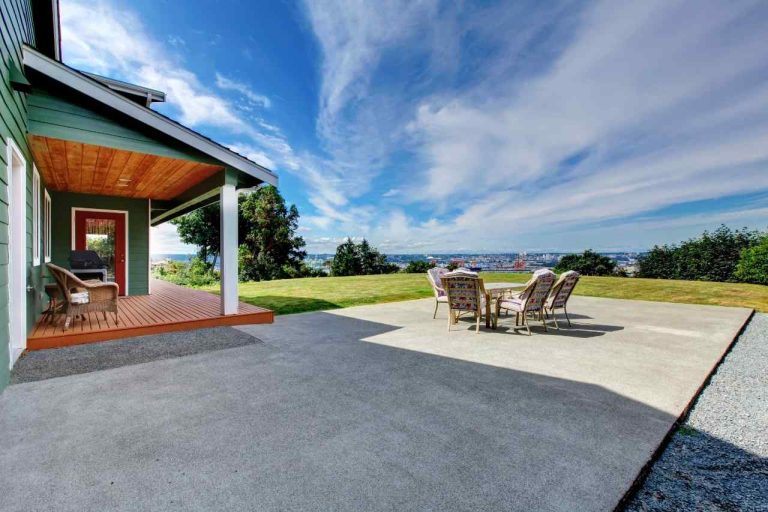 Modern house with a concrete patio featuring outdoor furniture, a wooden deck, and a scenic view of the city and sky in the background.