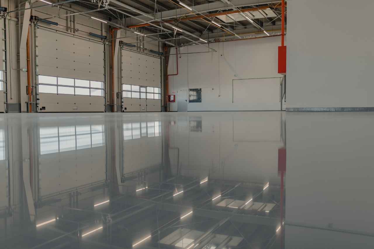 Newly finished industrial epoxy flooring inside a modern warehouse with high ceilings, roller doors, and reflective polished surface.