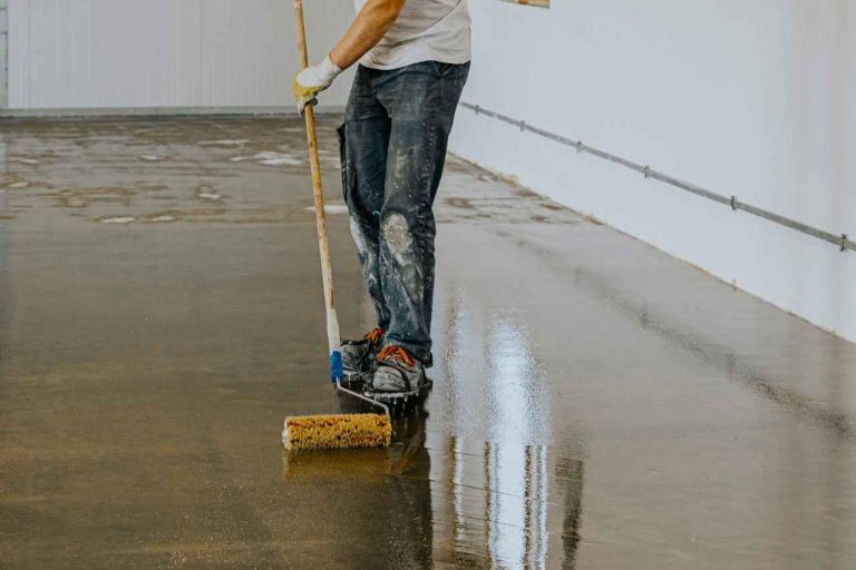 Worker applying epoxy coating on a concrete floor using a roller during industrial flooring installation.