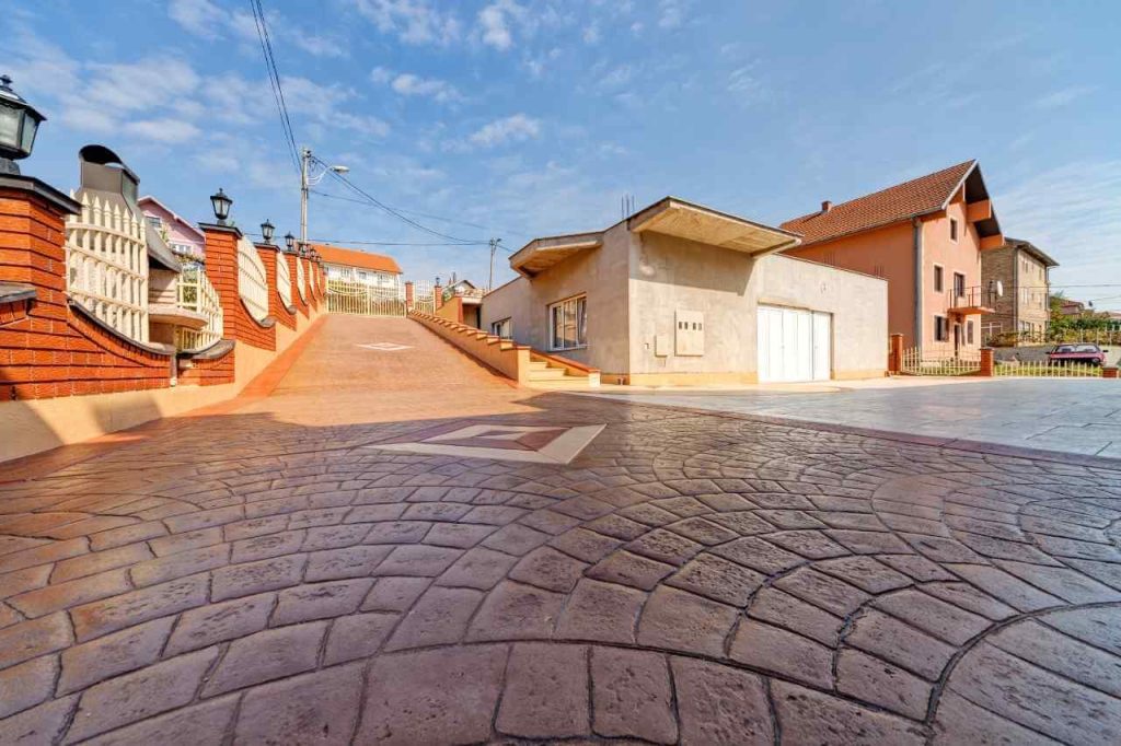 Decorative stamped concrete driveway with a circular pattern leading up to a modern house, surrounded by brick fences and a clear blue sky.